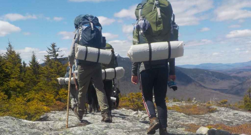 A group of backpackers cross rocky terrain toward mountains in the distance. 